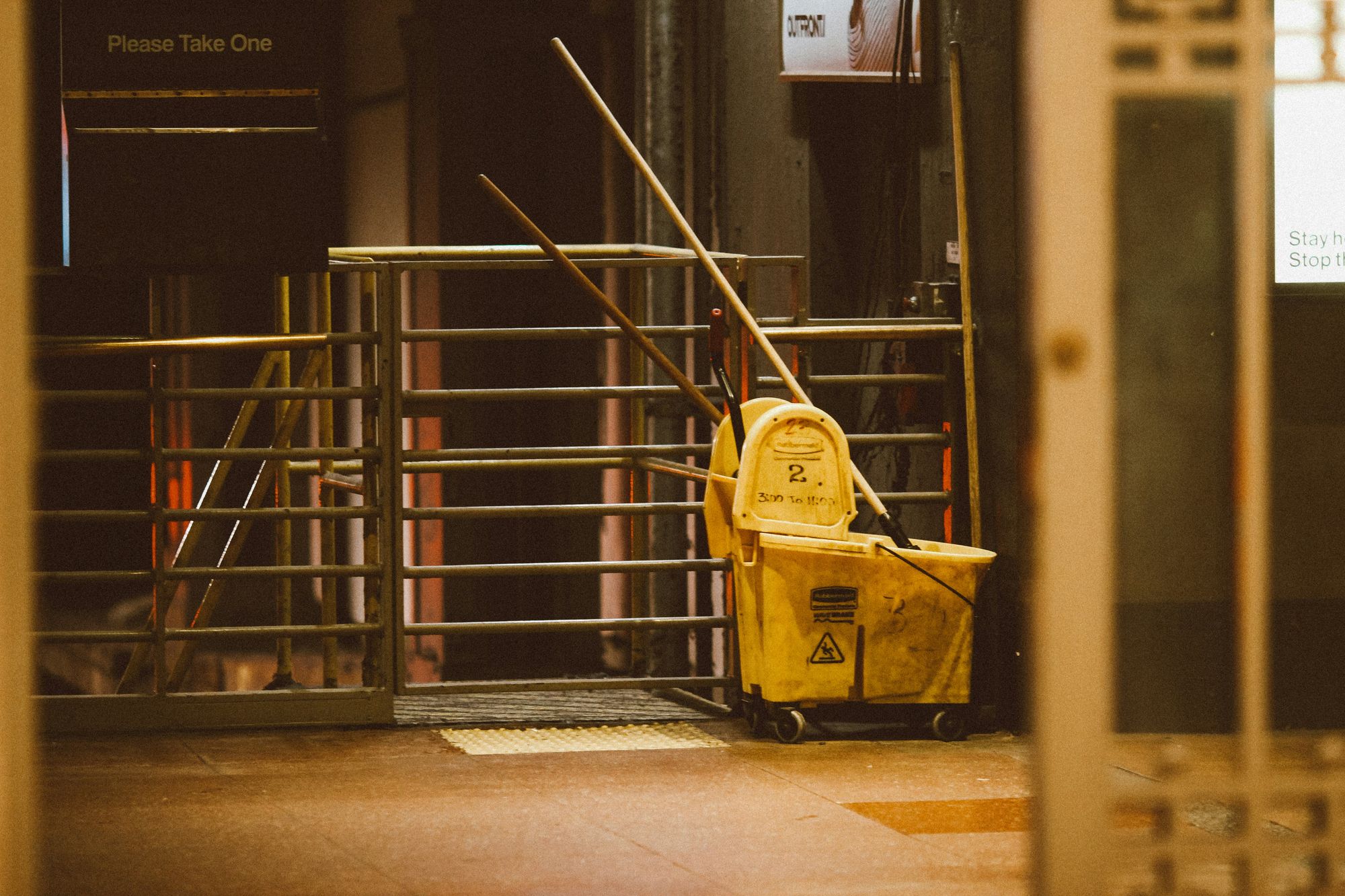 A janitor's mop bucket and mops left beside a service gate after hours